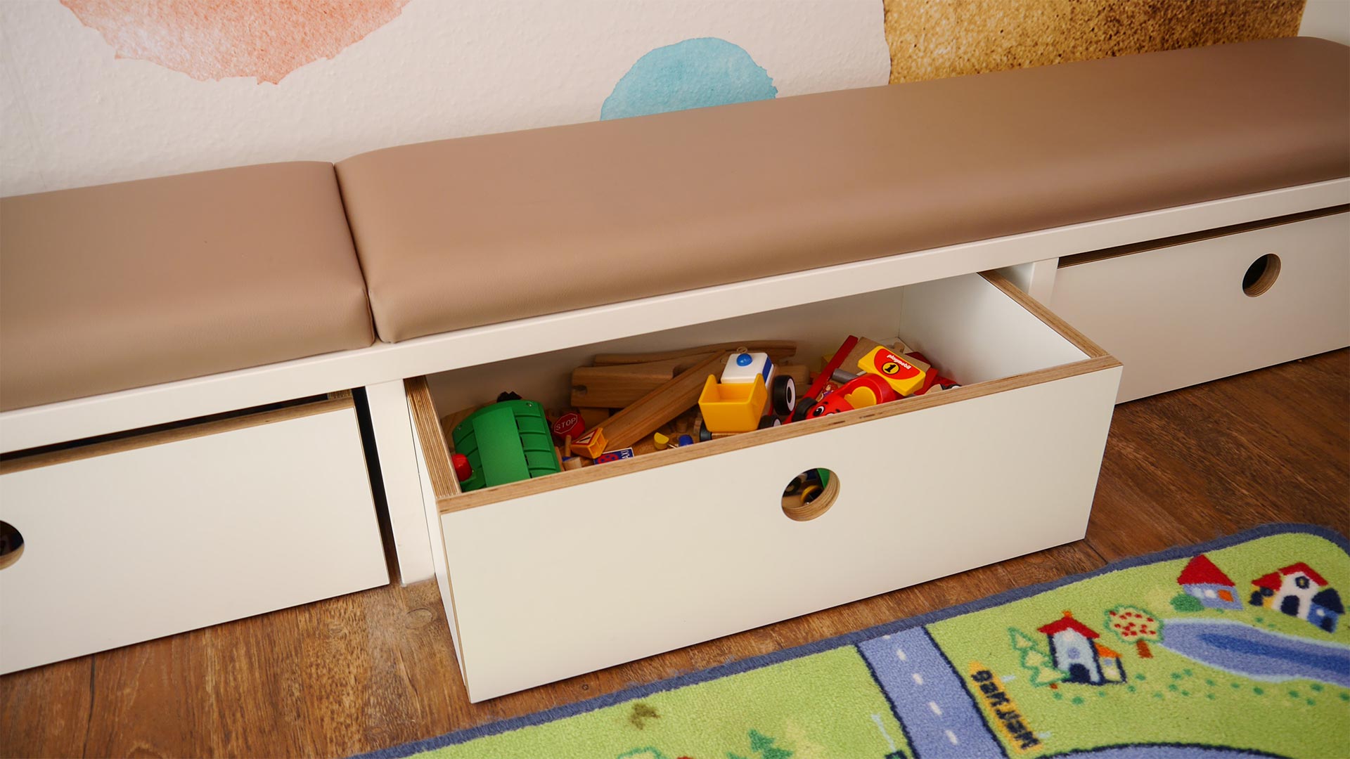 Unter den Kindersitzbänken im Wartezimmer befinden sich Spielzeugboxen.