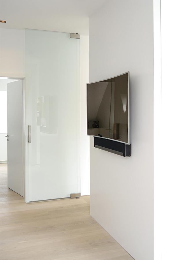 Auf der Rückseite des Trennwandmöbels ist ein TV-Gerät mit Soundbar aufgehängt