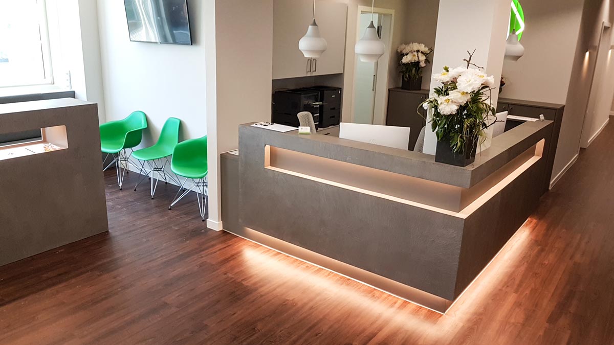 Der Eingangsbereich wird bestimmt von einer Empfangstheke in Beton-Optik mit indirekter LED-Beleuchtung